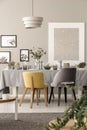 Grey and yellow chair at table under lamp in dining room interior