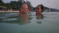 Greyhaired man and asian girlfriend look at each other in the water