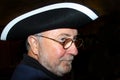 Greyhaired man with tricorn hat and round glasses and sly smile