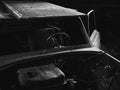 Greyscale closeup of an old car with dismantled parts in an old creepy room