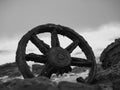 Greyscale closeup of an old rusty wheel surrounded by stones with a blurry background Royalty Free Stock Photo