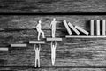 Greyscale image of small paper people holding up falling dominos while standing on wooden steps Royalty Free Stock Photo