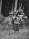 Greyscale of an old strong woman looking for grass to feed her goat in the forest