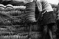 Greyscale of a person holding a stack of clay pots standing near the pots covered with woods