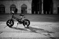 Greyscale shot of a four-wheel bicycle  parked in the middle of a square - childhood conception Royalty Free Stock Photo