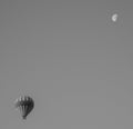 Greyscale shot of a hot air balloon in the sky with a half moon.