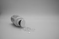 Greyscale shot of a lot of pills spilling out of a pill bottle on white background