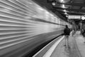 Greyscale shot of a man waiting for a train in the station and a blurred train in the motion