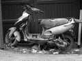 Greyscale shot of an old and abandoned motorcycle in the garbage