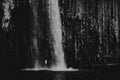Greyscale shot of a strong waterfall with a person standing below Royalty Free Stock Photo