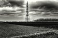 Greyscale shot of a tall metal radio tower in the middle of a countryside field under a cloudy sky Royalty Free Stock Photo