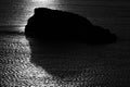 Greyscale silhouette of a rock in a sea under the sunlight