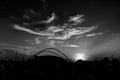 Greyscale of a wired bridge surrounded by people and greenery under a cloudy sky and sunlight Royalty Free Stock Photo