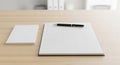 Black ballpoint pen resting on a blank grid paper notebook beside a stack of white paper sheets on a light wood desk Royalty Free Stock Photo