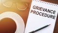 GRIEVANCE PROCEDURE text on notebook on office table with cup of coffee