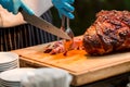 Grill restaurant kitchen. Chef in Blue cooking gloves using knife to cut smoked pork. Roast pork neck. Roasted shoulder of pork on Royalty Free Stock Photo
