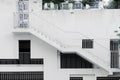 Grille windows of different shapes and sizes at white concrete wall, an external staircase on building, covered parking.