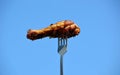 Grilled appetizing chicken leg on the fork against the blue sky. Outdoor barbecue