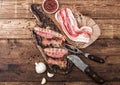 Grilled bacon strips on vintage wooden board with raw fresh smoked pork bacon on butchers paper with fork and knife on wooden