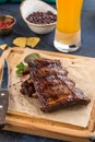 Grilled barbecue spareribs and bbq sauce on wooden board and glass of beer on blue background