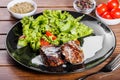 Grilled beaf steak meat with fresh vegetable salad and tomatoes on black plate, wooden background Royalty Free Stock Photo