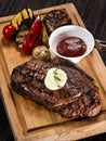 Grilled beef angus steak with melted butter on a wooden cutting board served with grilled vegetables, close up photo on a dark Royalty Free Stock Photo