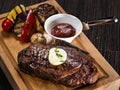 Grilled beef angus steak with melted butter on a wooden cutting board served with grilled vegetables, close up photo on a dark Royalty Free Stock Photo