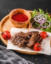 Grilled beef meat and vegetables with fresh salad and bbq sauce on cutting board over black stone background. Hot Meat Dishes Royalty Free Stock Photo