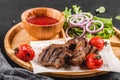 Grilled beef meat and vegetables with fresh salad and bbq sauce on cutting board over black stone background. Hot Meat Dishes Royalty Free Stock Photo