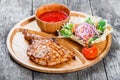 Grilled beef steak on bone, fresh salad, grilled vegetables and tomato sauce on cutting board on wooden background Royalty Free Stock Photo