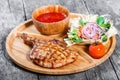 Grilled beef steak on bone, fresh salad, grilled vegetables and tomato sauce on cutting board on wooden background Royalty Free Stock Photo