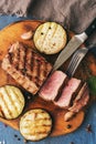 Grilled beef steak on a cutting board with vegetables, blue background. Top view, flat lay