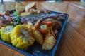 Grilled beef steak with gravy is served with a fruit and vegetable salad inside a black ceramic plate on the dining room table to Royalty Free Stock Photo