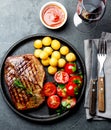 Grilled beef steak served on cast iron plate with tomato salad, potatoes balls and red wine. Barbecue, bbq meat beef Royalty Free Stock Photo