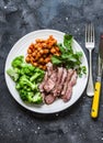 Grilled beef steak, spicy stewed chickpeas, broccoli - delicious healthy lunch on a dark background, top view