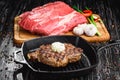 Grilled Black Angus Steak on grill iron pan on wooden black background with raw Royalty Free Stock Photo