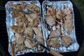 Grilled chicken breast slices placed on alluminium plates on grill, turned by steel forceps and fork during barbecue process.