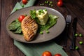 Grilled chicken fillet with mashed potatoes and green peas. Green tablecloth, dark woody background. Close-up view