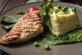 Grilled chicken fillet with mashed potatoes and green peas. Green tablecloth, dark woody background. Close-up view