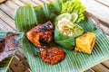 Grilled chicken with red barbecue sauce, vegetables and chili sauce served on banana leaves