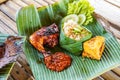 Grilled chicken with red barbecue sauce, vegetables and chili sauce served on banana leaves Royalty Free Stock Photo