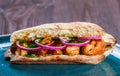 Grilled chicken in sandwich from fresh pita bread with onion and greens on dark wooden background.