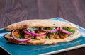 Grilled chicken in sandwich from fresh pita bread with onion and greens on dark wooden background.