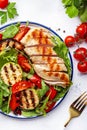 Grilled chicken and vegetables salad with spinach and arugula. Paprika, zucchini, eggplant, tomatoes on white table background, Royalty Free Stock Photo