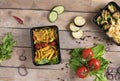 Two plastic containers with grilled chicken wings and raw vegetables on rustic background, vegetables salad and micro greens