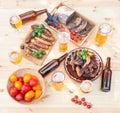 Grilled chicken wings, grilled sausages, glasses, mugs and bottles of beer, bread and bowl with tomatoes on wooden table. Top view Royalty Free Stock Photo