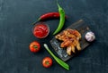 Grilled chicken wings on a wooden board with red sauce, onions, peppers and tomatoes. Dark background. Copy space Royalty Free Stock Photo