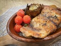 Grilled corvine with roasted cherry tomatoes and grilled artichoke, in an oven clay pot on a wooden board, mediterranean cuisine Royalty Free Stock Photo