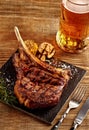 Grilled cowboy beef steak, glass of beer, herbs and spices on a wooden background. Top view. Royalty Free Stock Photo