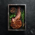 Grilled cowboy beef steak, herbs and spices on a black stone background. Barbecue. Top view.